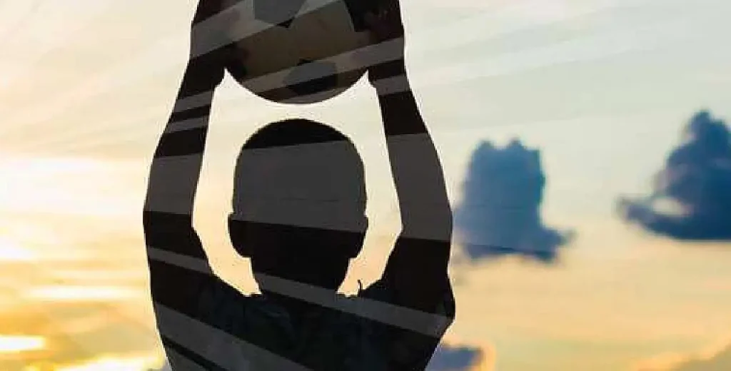 Silhouette of a young child holding a soccer ball with the suns rays coming from behind.